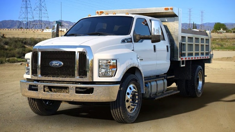 Oxford white Ford F-750 dump truck parked with mountains, trees, and metal poles in the background