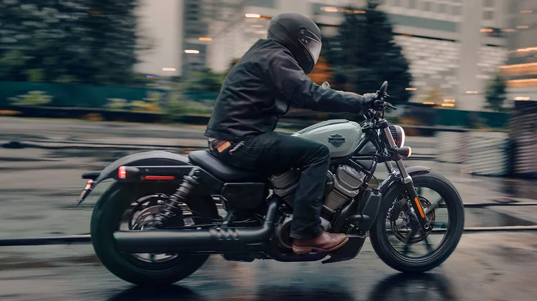 A helmeted rider cruises down a city street on a Harley-Davidson Nightster