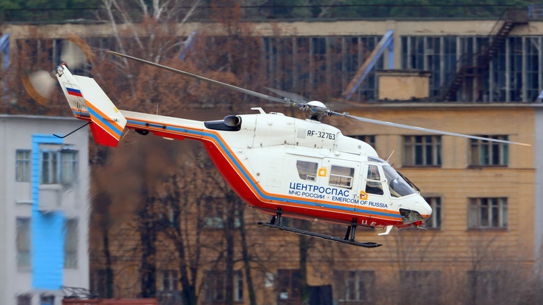 A red and white Kawasaki BK117 helicopter flying above a residential area