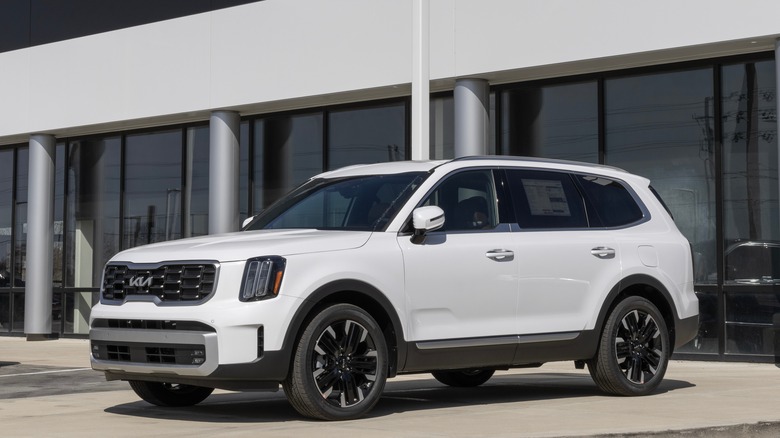 A white Kia Telluride outside a dealership, front 3/4 view