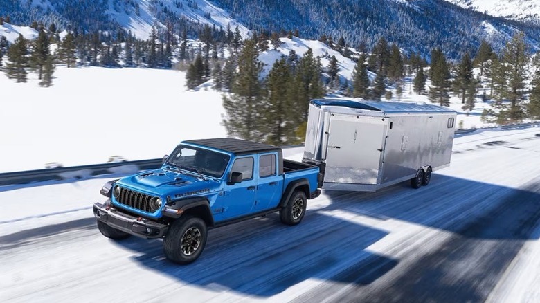 Blue and black 2025 Jeep Gladiator towing on a snowy road with trees and and snow-covered terrain in the background