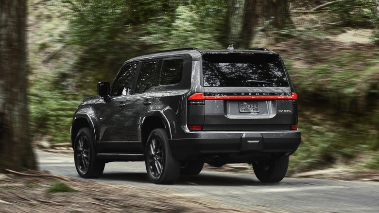 2024 Lexus GX Premium driving at speed through a road in the woods rear 3/4 view