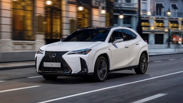 White 2025 Lexus UX driving down a city street with buildings in the background