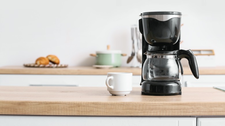 black coffee maker on the counter with a white coffee cup