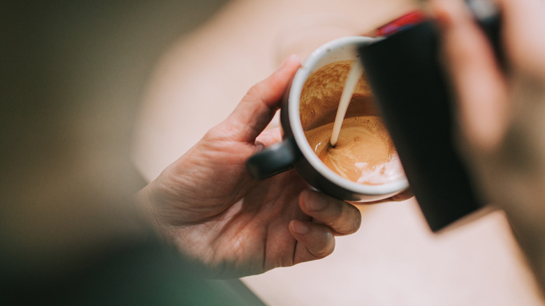 man pouring milk into a cup of coffee