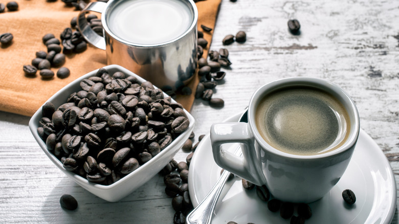 cup of coffee with milk on the side and coffee beans