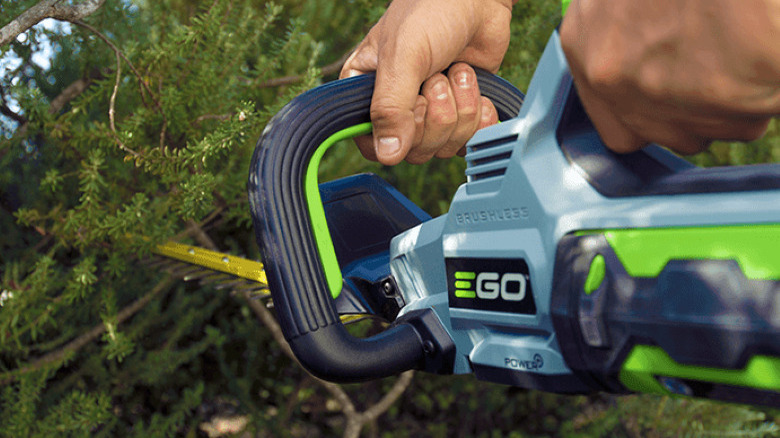 close up of person using hedge trimmer on bushes