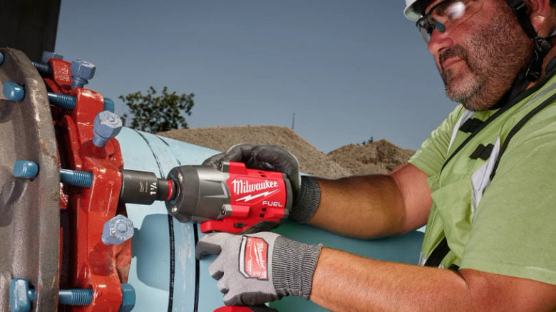 Person using Milwaukee impact wrench on large pipe fasteners