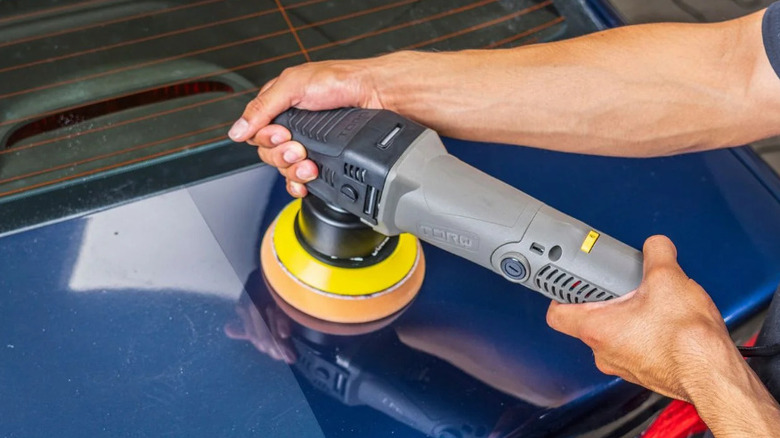 Person using polisher on a blue car trunk