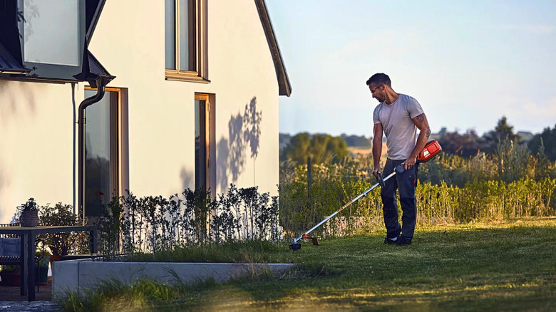 A man using a Husqvarna string trimmer to cut grass.