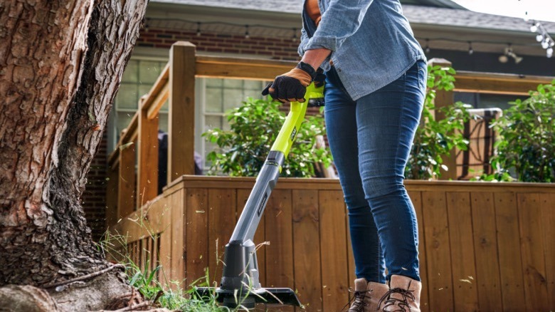 A woman at work in the garden using a Ryobi grass trimmer.