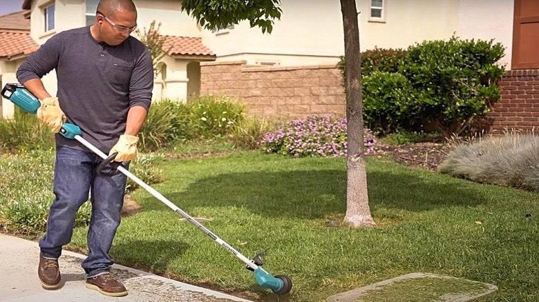 A man edging a lawn with a Makita string trimmer