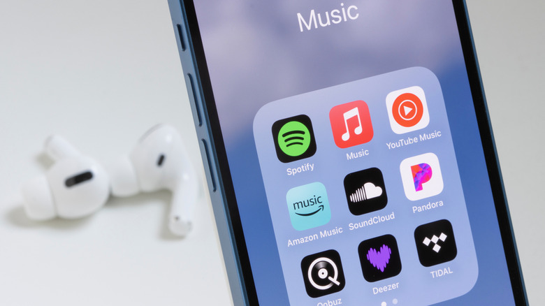 An iPhone displaying multiple music streaming apps with AirPods in the background