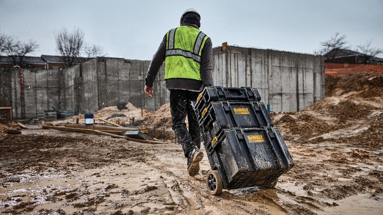 Person pulling Dewalt toolboxes across mud