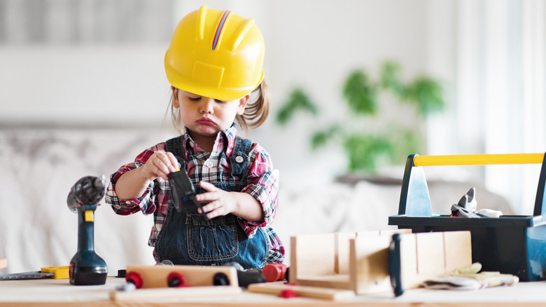 Kid in hard hat playing with toy tools