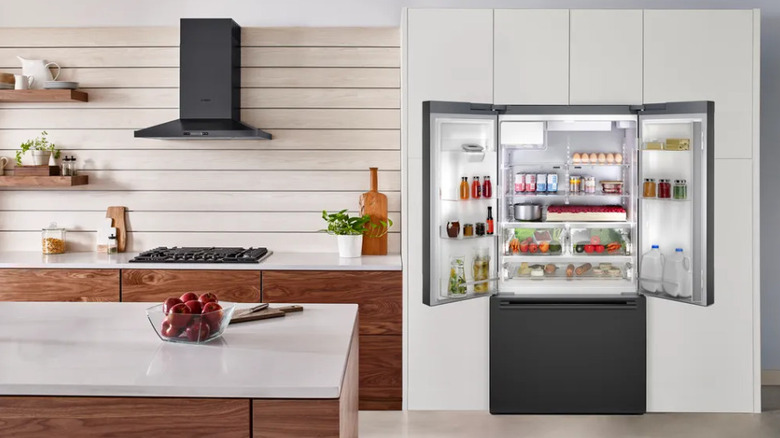 An open grey fridge in a white kitchen with wood cabinets