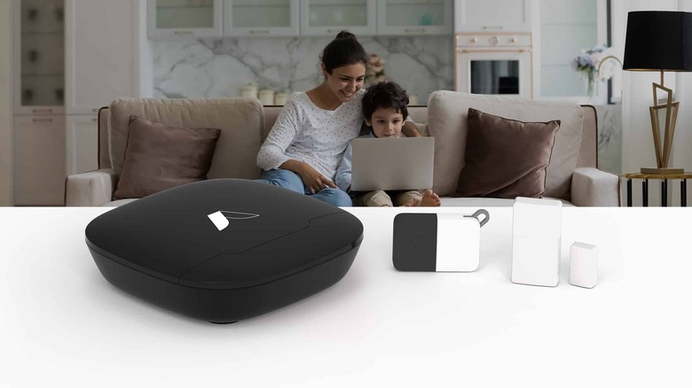 The Security Kit featuring various Abode products on a table, a woman and a child sit on a sofa behind.