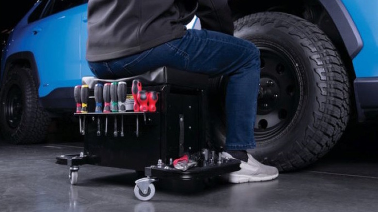 Person sitting on tool cart seat in front of car wheel