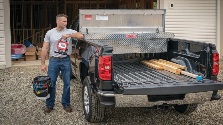 Person with bucket next to pickup with lumber and toolbox in bed