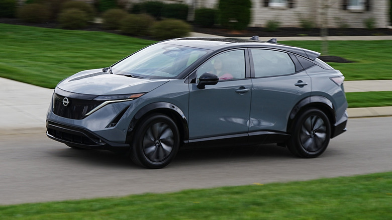 Nissan Ariya Platinum+ e-4ORCE driving down a road with green grass on either side