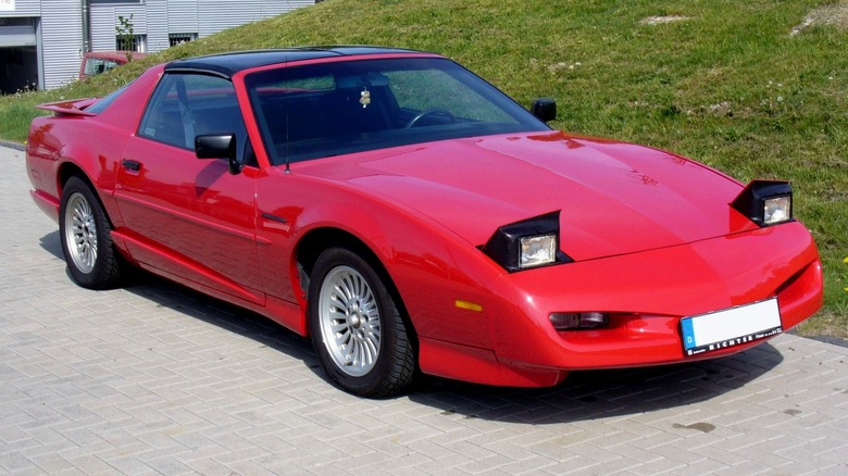 Red third-generation Pontiac Firebird parked with lights up