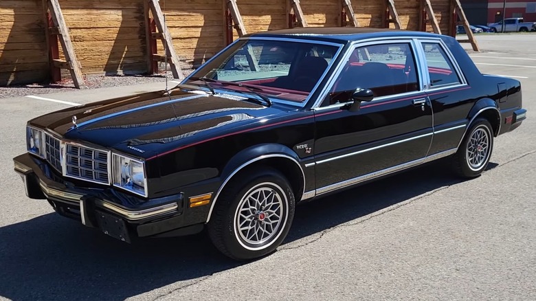 Black Pontiac Phoenix LJ parked in front of wooden barrier