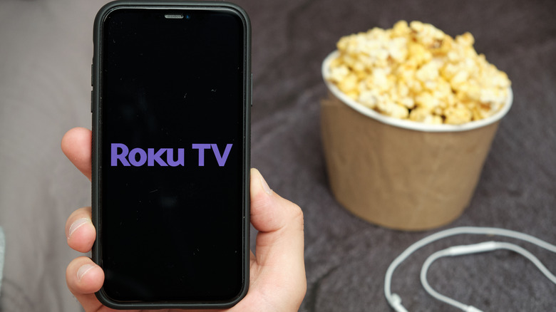 Roku TV app on phone alongside popcorn and earbuds