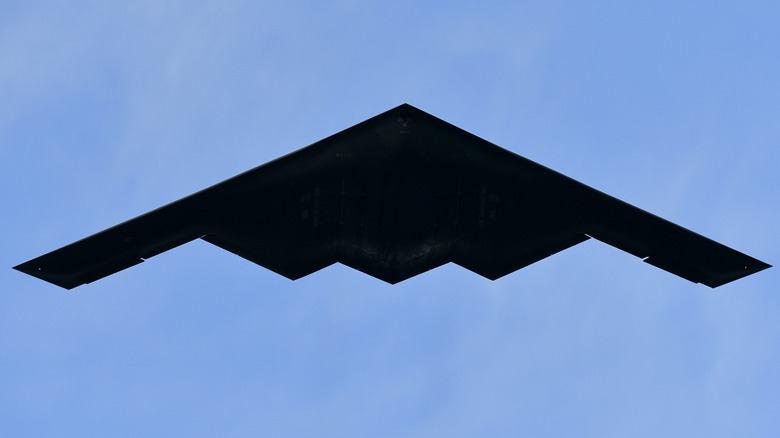 A B-2 Spirit flying over blue skies as seen from below