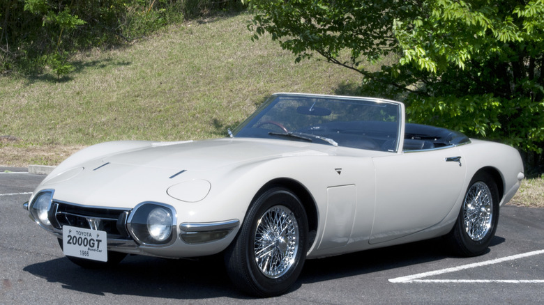 A white Toyota 2000GT Convertible parked in front of a grassy slope.