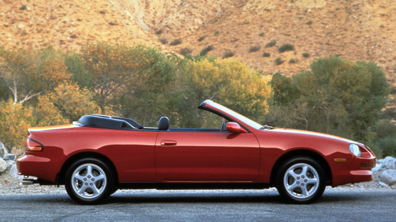 A red 1999 Toyota Celica Convertible on a road, in front of scrub and desert.