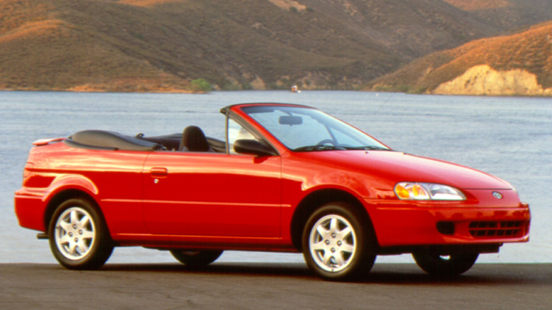 A red 1997 Toyota Paseo Convertible in front of water and hills.