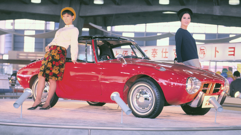 A red Toyota Sports 800 with two women modeling near it at an auto show.