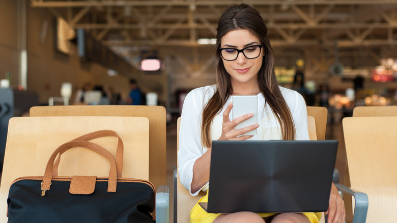 A women with eyeglasses using her phone and laptop while waiting for her flight