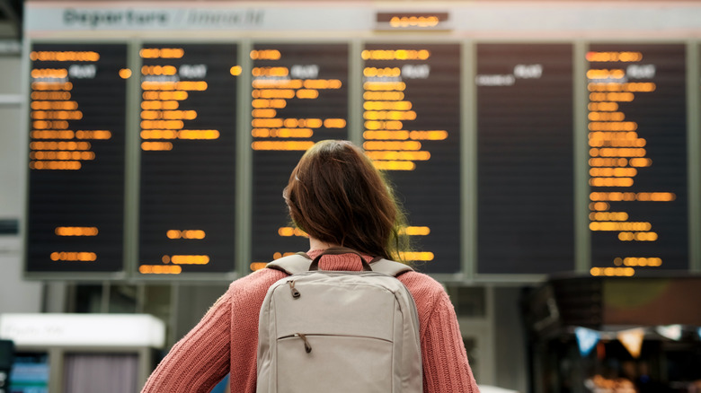 A young female wearing a carry-on bag while checking the flight schedule at the airport