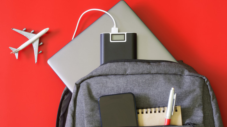 A toy plane placed beside a traveler's backpack loaded with devices and items, including a laptop, power bank, smartphone, notepad and a pen