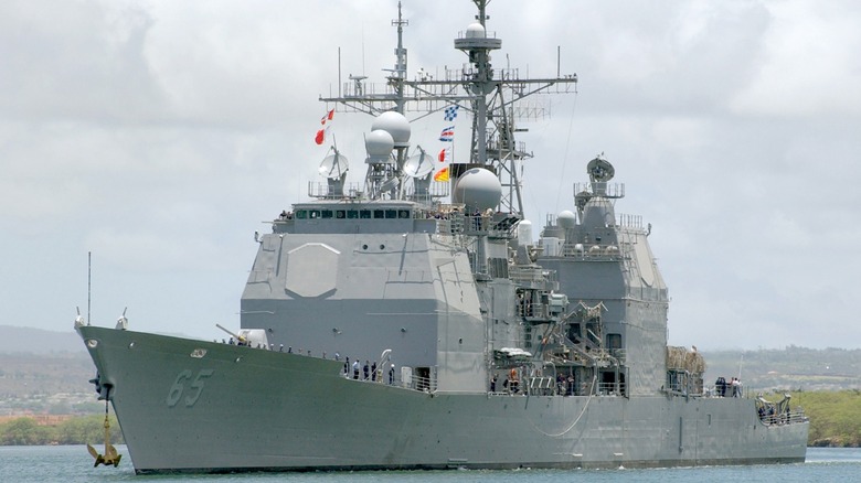 The USS Chosin (CG-65) near the shore with Navy personnel standing at attention on the deck