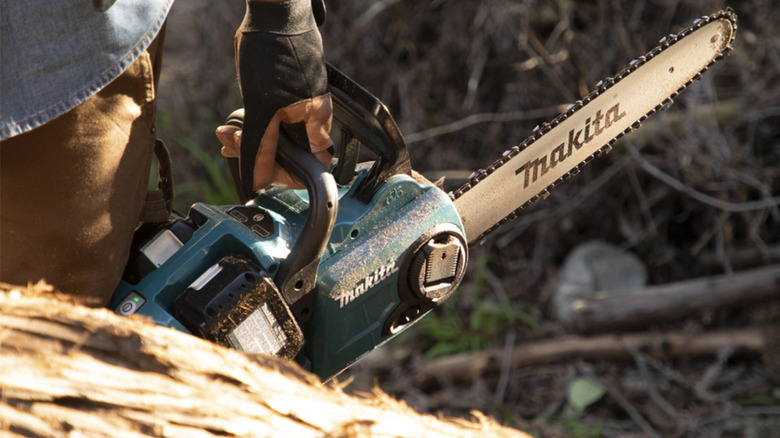 Person holding a Makita chainsaw outside