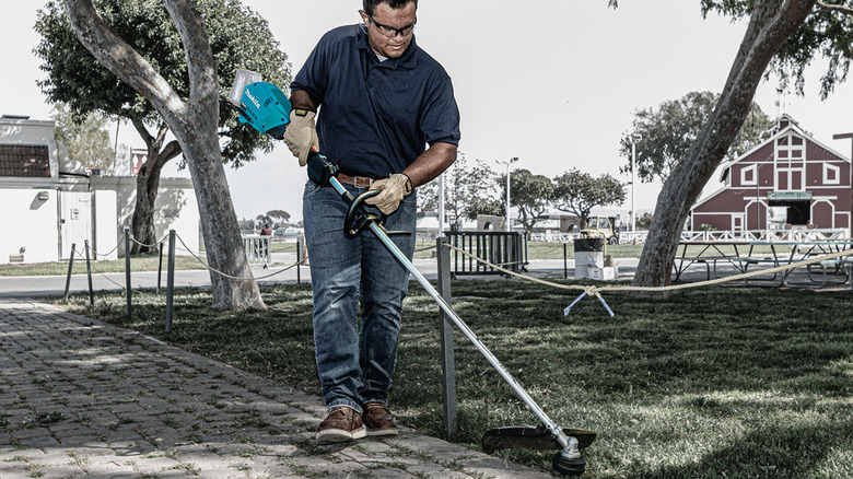 Man using a string trimmer to cut grass 