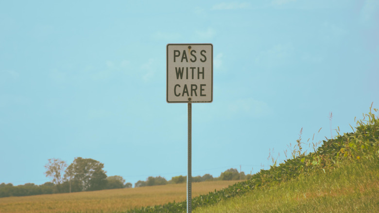 Pass With Care sign installed with greenery in the background