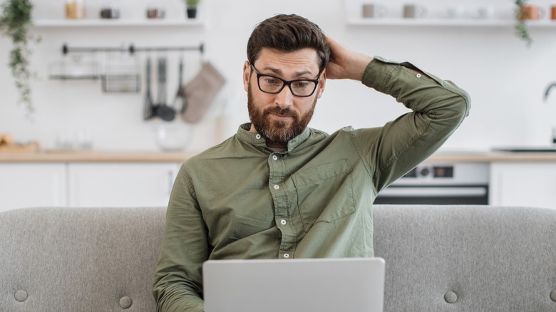 Man scratching head while looking at laptop