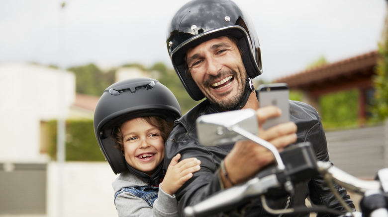 child and father on motorcycle taking a selfie