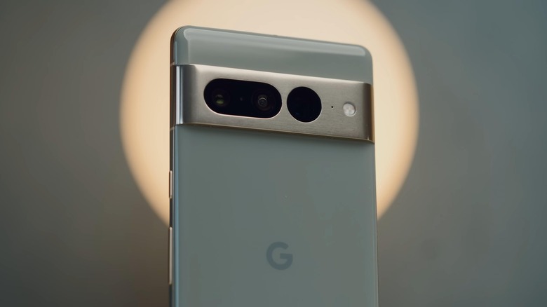 Google Pixel 7 Pro in sand green colorway, held against a source of circular light halo.