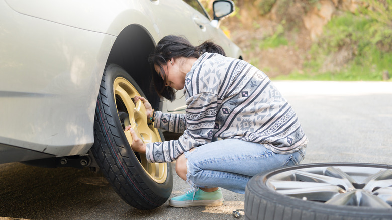 A woman putting a spare tire on