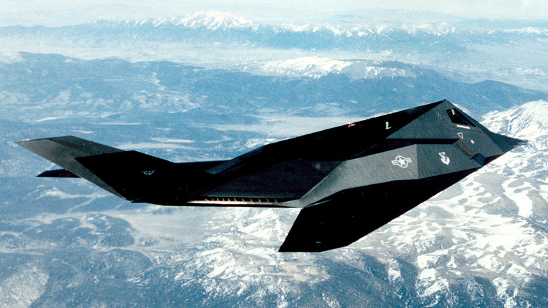 A F-117 Nighthawk soars above a mountainscape