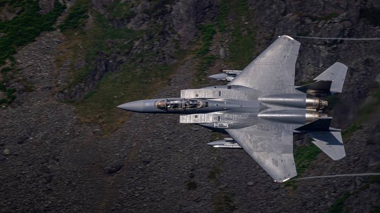 A birds-eye-view of an F-15E Strike Eagle flying low over a valley