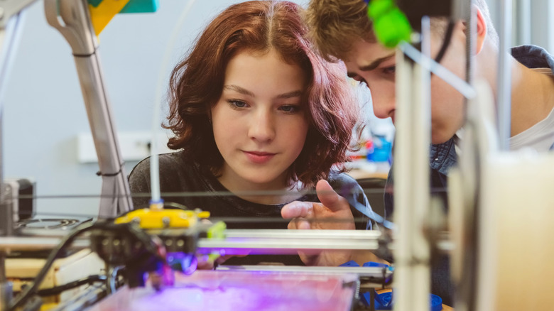 Two teens work with a 3D printer