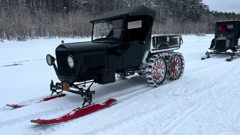 A MOdel T Snowmobile with front skis and caterpillar tracks driving through the snow.