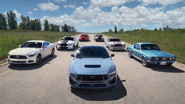 Multiple generations of Ford Mustangs parked on a road