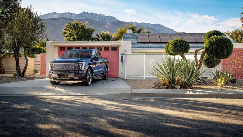 F-150 Lightning plugged in in front of home with solar panels