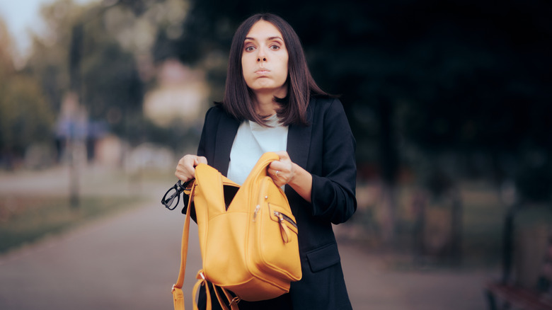 Woman on a street looking in her messy backpack